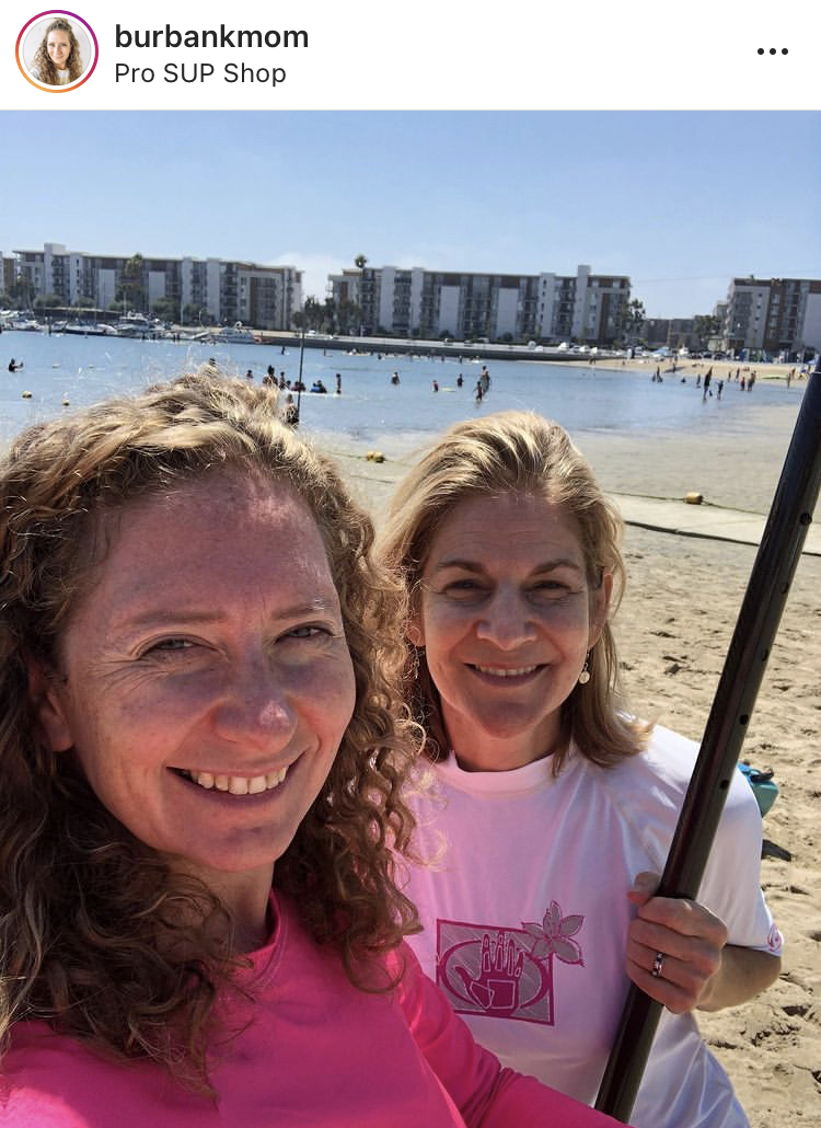 two friends smiling with beach and water in background