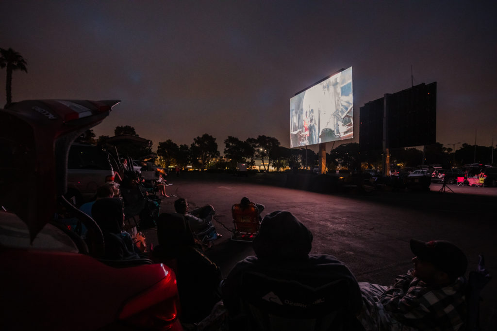 People sitting in lawn chairs and cars watching drive-in movie in Marina del Rey