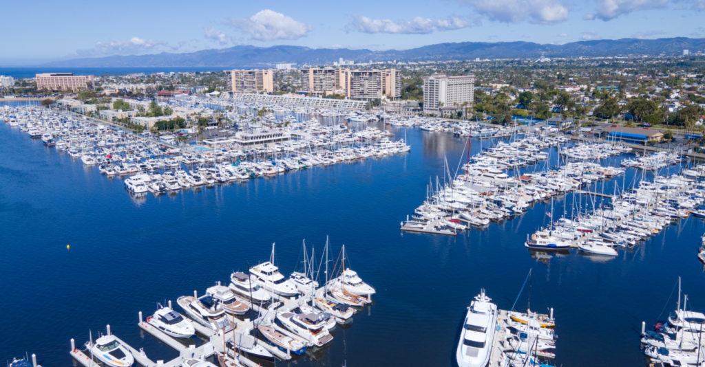 Aerial view above Marina del Rey channel with boats and hotels and buildings with Santa Monica Mountain range in background