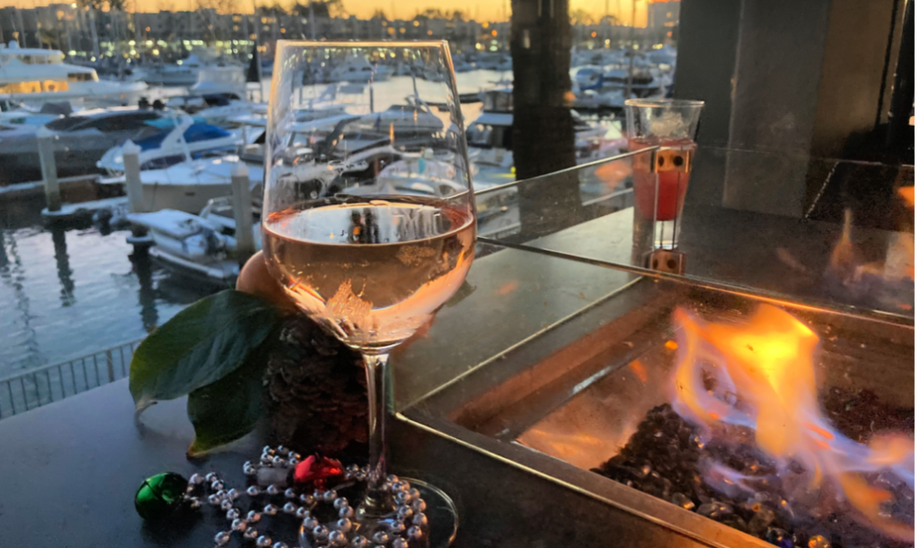 Wine glass on firepit table next to harbor and boats during sunset